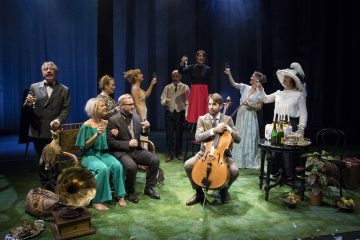 Joukko viralliseen ja vintage-vaatetukseen pukeutuneita ihmisiä kokoontuu nurmikolla sijaitsevalle lavalle, osa istuu ja osa seisoo ja kohottaa maljoja. Mies soittaa selloa, ja näyttämöä koristavat rekvisiitta, kuten gramofoni ja kynttilänjalat.