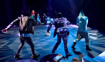 Värikkäisiin, eklektisiin pukuihin pukeutuneet esiintyjät tanssivat energisesti näyttämöllä dramaattisessa valaistuksessa, ja rekvisiittaa oli ripoteltu ympäriinsä, ja yleisö näkyi hädin tuskin varjoissa.