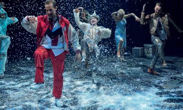 Viisi esiintyjää tanssii tarmokkaasti keinolumella päällystetyllä lavalla, ja heidän ympärilleen putoaa konfetteja. Heillä on värikkäät ja tyylikkäät puvut, ja kukin heistä on vangittu kesken liikkeen kirkkaaseen näyttämövalaistukseen.