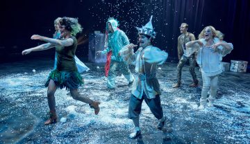Kuusi värikkäisiin pukuihin pukeutunutta esiintyjää esiintyy lumen peittämällä lavalla, ja heidän ympärilleen putoaa keinolunta. He näyttävät olevan keskellä tanssia tai juoksemassa, mikä luo energisen ja omituisen tunnelman.