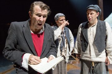 Lavalla esiintyy kolme näyttelijää kuluneissa, vanhanaikaisissa vaatteissa. Edessä oleva mies kirjoittaa muistikirjaan ja näyttää yllättyneeltä tai ahdistuneelta, kun taas hänen takanaan olevat kaksi näyttelijää vaikuttavat huolestuneilta, toinen pitää kättä kasvojensa lähellä.