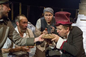 Neljä vanhanaikaisiin, riekaleisiin vaatteisiin pukeutunutta miestä kerääntyy innokkaasti ympärilleen, kun yksi punahattupäinen mies haistelee nälkäisenä pyöreää leipää tai valmistautuu syömään sitä, kun taas toinen mies ojentaa makkaraa. Kohtaus vaikuttaa teatraaliselta ja dramaattiselta.