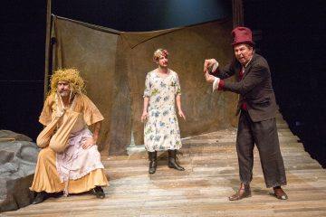 Lavalla esiintyy kolme näyttelijää leikkisissä puvuissa: yhdellä on olkiperuukki ja keltainen mekko, toisella kukkamekko ja kukkapäähine, ja kolmannella on puku ja punainen hattu, ja hän elehtii dramaattisesti. Lavastus muistuttaa maalaismaista, puista näyttämöä.