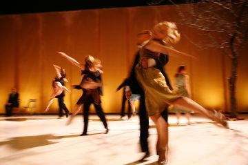 Ryhmä tanssijoita esiintyy tarmokkaasti lämpimästi valaistulla lavalla, yksi pari etualalla keskellä nostoa. Liikkeen epätarkkuus korostaa heidän liikettään ja sirouttaan. Oikealla puolella seisoo paljas puu.