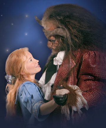 Siniseen mekkoon pukeutunut nainen hymyilee ja katselee suurta, punatakkista, petomaista hahmoa, joka tanssii yhdessä tummansinistä, tähtitaivasta vasten.