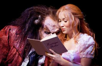 Petopukuinen mies ja vaaleanpunaiseen mekkoon pukeutunut nainen istuvat tiiviisti vierekkäin ja lukevat