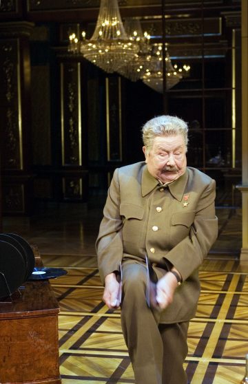 Ruskeaan sotilaspukuun ja mitaleihin pukeutunut näyttelijä esiintyy tarmokkaasti puisella näyttämöllä nostamalla yhtä polvea ja pitelemällä näkymättömiä ohjaksia koristeellisessa huoneessa suuren kattokruunun alla.