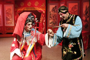 Lavalla esiintyy kaksi esiintyjää värikkäissä, taidokkaissa kiinalaisissa oopperapuvuissa. Toinen istuu punaisessa puvussa, jossa on koristeellinen päähine ja huntu, ja näyttää ahdistuneelta, kun taas toinen seisoo mustassa ja sinisessä puvussa ja osoittaa heitä dramaattisesti.