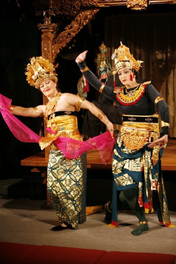 Lavalla esiintyy kaksi tanssijaa perinteisissä balilaisissa puvuissa ja koristeellisissa kultaisissa päähineissä, joista toisella on kädessään vaaleanpunainen huivi. Taustalla on taidokkaita puuveistoksia ja toinen esiintyjä puvussa.