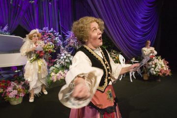 Lavalla esiintyy kolme ihmistä taidokkaissa, värikkäissä puvuissa kukka-asetelmien ja violettien verhojen ympäröimänä. Yksi henkilö laulaa intohimoisesti etualalla, kun taas kaksi muuta seisoo takana, toinen pitelee kukkia.