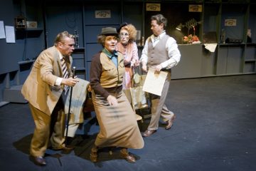 Neljä vintage-asuihin pukeutunutta näyttelijää esiintyy juna-asemaa muistuttavassa lavastuksessa matkalaukkuja ja rekvisiittaa kädessään, ja heidän dramaattiset ilmeensä ja kehonkielensä viittaavat kiireeseen tai hämmennykseen.