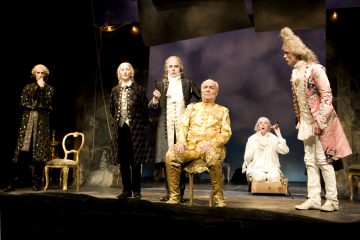 Lavalla esiintyy kuusi näyttelijää koristeellisissa 1700-luvun puvuissa; yksi istuu kuninkaallisesti kultaisessa puvussaan, kun taas muut, mustiin tai valkoisiin pukeutuneet, seisovat tai istuvat hänen ympärillään dramaattisessa valaistuksessa.