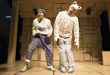 Lavalla esiintyy kaksi leikkisästi pukeutunutta ihmistä; toisella on pipo, collegepaita ja kuviolliset housut, kun taas toisella on valkoinen hattu, jossa on karhunkorvat, ja X-kirjaimilla varustettu pusero, ja hän seisoo pahvilaatikoiden taustaa vasten.