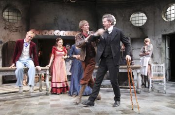 Ryhmä aikakauden pukuihin pukeutuneita näyttelijöitä esiintyy näyttämöllä; kaksi miestä on jännittyneessä yhteenotossa muiden katsellessa, joka tapahtuu maalaismaisessa, vanhanaikaisessa huoneessa, jossa on kuluneet huonekalut ja pyöreät ikkunat.