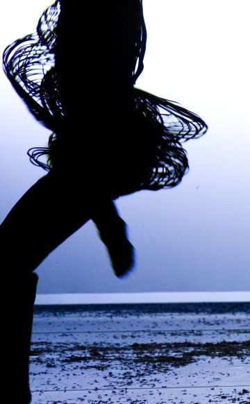 Siluetti henkilöstä, joka on liikkeessä ja jolla on vyötärönsä ympärillä pyöriviä muotoja luova vaijeri- tai rengashame, kirkkaalla taustalla, jossa on näkyvä lattia.