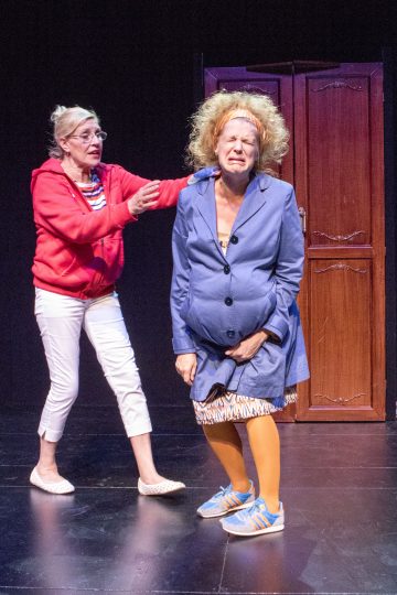 Lavalla esiintyy kaksi näyttelijää; toinen, jolla on punainen huppari, valkoiset housut ja silmälasit, elehtii kiireesti kohti toista, jolla on sininen takki, oranssit sukkahousut ja sotkuinen tukka ja joka näyttää ahdistuneelta puisen vaatekaapin edessä.