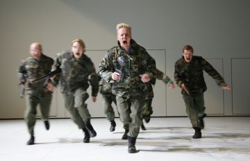 Viisi naamioasuihin pukeutunutta ihmistä juoksee eteenpäin intensiivisin ilmein, ikään kuin huutaen. Tausta on yksivärinen ja valkoinen, ja he näyttävät olevan lavalla tai valoisassa sisätilassa.