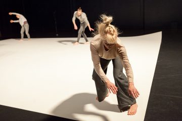 Kolme neutraalisävyisiin vaatteisiin pukeutunutta paljasjalkaista tanssijaa tekee ilmeikkäitä, nykyaikaisia liikkeitä valkoisella näyttämöllä, jossa on tumma tausta. Edessä oleva tanssija kumartuu eteenpäin, kun taas kaksi takana olevaa tanssijaa liikkuvat ojennetuin käsin.