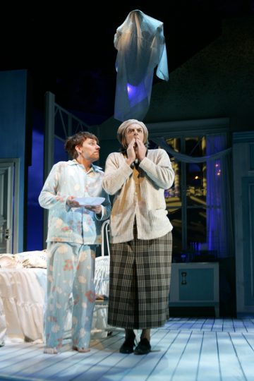 Kaksi pyjamaista ja yömyssyyn pukeutunutta näyttelijää seisoo kirkkaasti valaistussa makuuhuoneessa ja katsoo hermostuneena heidän yläpuolellaan leijuvaa valkoiseen kankaaseen verhottua aavemaista hahmoa. Kohtaus viittaa komedialliseen tai aavemaiseen teatteriesitykseen.