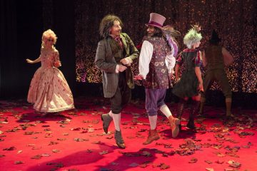 Neljä näyttelijää värikkäissä, taidokkaissa puvuissa esiintyy lehdillä peitetyllä punaisella näyttämöllä. Kaksi tanssii yhdessä keskellä, kun taas muut, mukaan lukien vaaleanpunaiseen aikakauden mekkoon pukeutunut nainen, ovat taustalla.