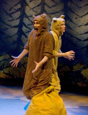 Lavalla esiintyy kaksi karhupukuista ihmistä. Toisella on yllättynyt ilme kädet ojennettuina, kun taas toinen näyttää vakavalta; heidän takanaan on maalattu metsätausta.