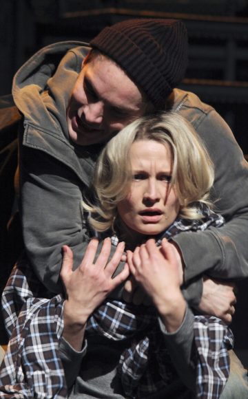 Tummaan huppariin ja pipoon pukeutunut henkilö pidättelee väkisin takaapäin ahdistunutta naista pitelemällä tämän niskasta ja hartioista kiinni. Nainen vaikuttaa pelästyneeltä ja tarttuu häntä pidelleisiin käsivarsiin.