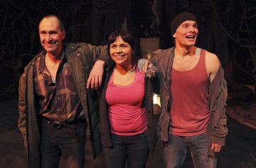 Kolme ihmistä seisoo yhdessä hymyillen. Vasemmalla olevalla miehellä on ruudullinen paita ja vihreä takki, keskellä olevalla naisella vaaleanpunainen toppi ja oikealla olevalla miehellä pipo, toppi ja takki. He vaikuttavat iloisilta ja rennoilta.