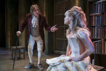 Vanhempi mies, joka on pukeutunut aikakauden vaatteisiin, elehtii keppi kädessään ja puhuu nuorelle naiselle, joka istuu kevyessä, tyylikkäässä puvussaan ja jolla on avoin kirja sylissään, kirjahyllyjen ympäröimänä hämärästi valaistulla näyttämöllä.