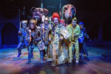 Lavalla esiintyy kuusi näyttelijää värikkäissä, omalaatuisissa puvuissa ja meikeissä; kahdella on suuret eläimelliset päähineet, ja yhdellä on kirkkaanpunaiset hiukset. Kohtaus on eläväinen ja teatraalinen, ja siinä on dramaattinen valaistus ja ilmeikkäät asennot.