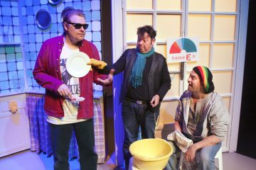 Kolme miestä värikkäässä keittiöympäristössä esittää komediallisen kohtauksen. Yhdellä on aurinkolasit ja hänellä on lautanen kädessään, toinen elehtii kohti, ja kolmas, jolla on raidallinen pipo, istuu keltaisen altaan ääressä. Heidän takanaan näkyy France 2 -kyltti.