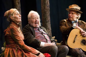 Ulkona penkillä istuu kolme vanhaa ihmistä, joilla on vintage-vaatteet: oranssipukuinen nainen, raitapaitainen mies, joka keskustelee vilkkaasti, ja toinen hattupäinen mies, jolla on kädessään kitara. Taustalla on puita.