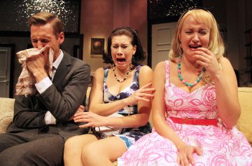 Kolme ihmistä istuu sohvalla, kaikki silminnähden järkyttyneitä ja itkeviä. Vasemmalla istuva mies pyyhkii kasvojaan nenäliinalla, kun taas hänen vieressään olevilla kahdella naisella on ahdistuneet ilmeet ja kyyneleet kasvoillaan.