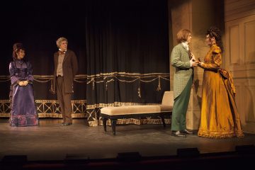 Neljä viktoriaanisen ajan pukuihin pukeutunutta näyttelijää esiintyy lavalla. Kaksi naista, toinen purppuranpunainen ja toinen kultainen, ovat vastakkain oikealla, kun taas kaksi muuta, mies ja nainen, katselevat vasemmalta, keskellä on penkki.