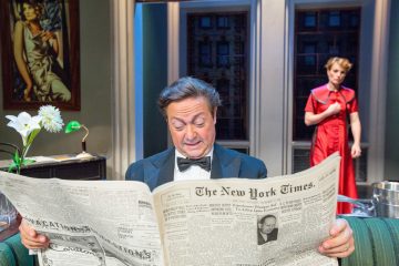 Smokkiin pukeutunut mies lukee New York Times -lehteä kirkkaasti valaistussa huoneessa, kun punamekkoon pukeutunut nainen seisoo taustalla huolestuneen näköisenä. Hänen vieressään pöydällä on maljakko, jossa on valkoisia kukkia, ja maalaus.