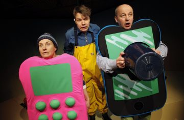 Kolme pukumiestä: yksi kirkkaan vaaleanpunaisessa laskentapuvussa, toinen keltaisessa vedenpitävässä haalarissa ja kolmas vihreämustassa älypuhelinpuvussa, jotka kaikki näyttivät yllättyneiltä tai huolestuneilta.