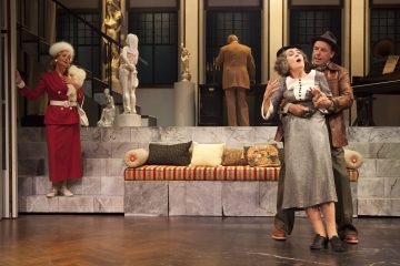 Kolme näyttelijää esiintyy näyttämöllä, joka muistuttaa tyylikästä olohuoneen veistoksia. Yksi punapukuinen nainen seisoo vasemmalla, kun taas mies pidättelee toista naista näyttämön keskellä. Neljäs henkilö seisoo takana, kasvot poispäin.