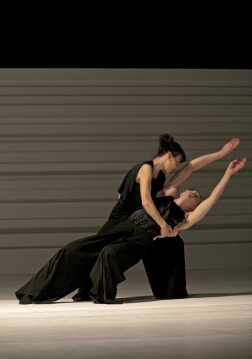 Kaksi mustiin asuihin pukeutunutta tanssijaa esittää nykyaikaisen dueton; toinen nojaa taaksepäin toisen tukemana, ja molemmat ojentavat kätensä ylöspäin ilmeikkäästi raidallista taustaa vasten.