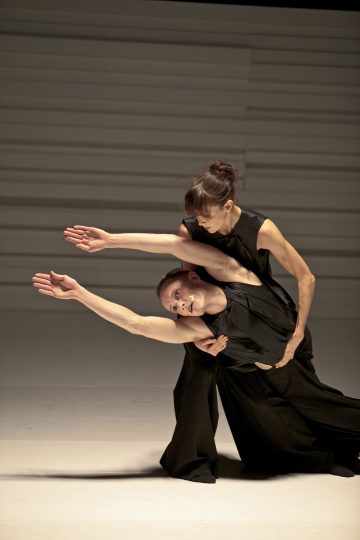 Kaksi mustiin asuihin pukeutunutta nykytanssijaa esittää ilmeikkään asennon; toinen nojaa eteenpäin ojennetulla kädellä, kun taas toinen tukee takaapäin, molemmilla on keskittynyt ilme. Tausta on minimaalinen ja neutraali.