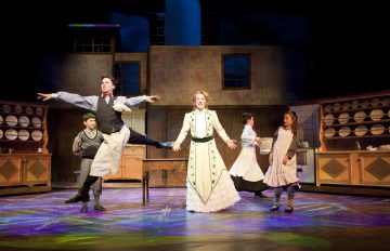 Viisi näyttelijää esiintyy kirkkaasti valaistulla, keittiötä muistuttavalla näyttämöllä, jossa yksi henkilö hyppii iloisesti, kun taas muut seisovat tai kävelevät. Lavastuksessa on astiahyllyjä, pöytä ja keittiön kaappeja taustalla.