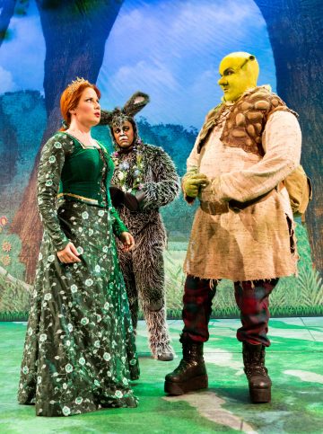 Lavalla esiintyy kolme näyttelijää: yksi prinsessa Fiona vihreässä mekossa, yksi Aasi karvaisin korvin ja hännin ja yksi Shrek vihreässä meikissä ja örkkiasussa metsätaustalla.