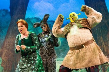 Lavalla esiintyy kolme värikkäisiin pukuihin pukeutunutta näyttelijää: yksi on Shrek vihreässä meikissä, toinen on Aasi karvaisessa puvussa ja kolmas Fiona vihreässä mekossa, ja he kaikki tekevät ilmeikkäitä ilmeitä ja eleitä metsäistä taustaa vasten.