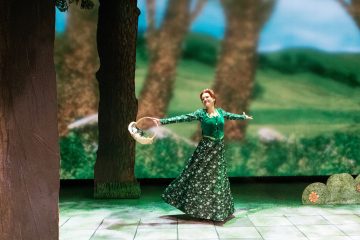 Pitkään, vihreään kukkamekkoon pukeutunut nainen tanssii sulavasti lavalla, jonka taustalla on metsä, ja pitää koria sivussaan. Puut ja vehreys ympäröivät häntä, mikä luo omituisen, satumaisen tunnelman.