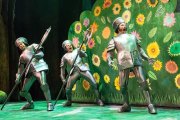 Lavalla esiintyy kolme näyttelijää kiiltävissä ritariasuissa. He seisovat värikkään, suurista kukista ja lehdistä koostuvan taustan edessä keihäät kädessään ja kypärät päässään, ja vaikuttavat eloisilta ja ilmeikkäiltä.