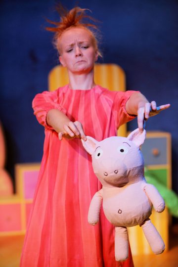 Vaaleanpunaiseen mekkoon pukeutunut nainen pitelee pehmopossua.