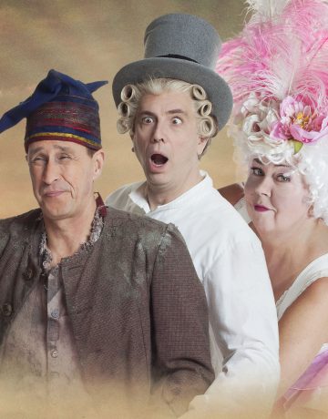 Kolme teatteripukuista henkilöä poseeraa yhdessä. Yhdellä on maalaisasu ja lippalakki, toisella valkoinen paita, harmaa silinterihattu ja valkoinen kiharaperuukki, ja kolmannella on valkoinen mekko ja vaaleanpunaisilla höyhenillä koristeltu pitkä peruukki.