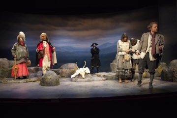 Teatterikohtauksessa on kuusi näyttelijää aikakauden puvuissa kallioisella näyttämöllä, jonka taustalla on pilvinen tausta. Kaksi hahmoa seisoo vasemmalla värikkäissä asuissa, kolme on oikealle sidottuina synkät ilmeet, ja yksi mustiin pukeutunut seisoo takana.