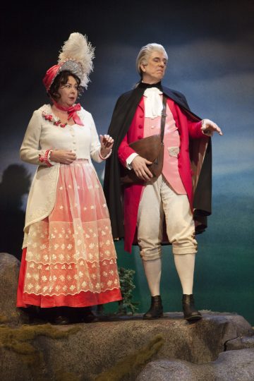 Lavalla seisoo kaksi näyttelijää, joilla on taidokkaat 1700-luvun puvut. Naisella on vaaleanpunainen ja valkoinen mekko, jossa on suuri höyhenpäähattu, ja miehellä on punainen takki, valkoiset housut, musta viitta ja valkoinen peruukki.