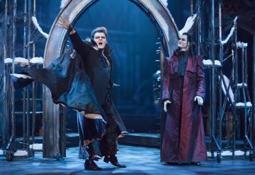 Kaksi dramaattisiin vampyyriasuihin pukeutunutta esiintyjää toimii näyttämöllä, jossa on goottilaisia kaaria ja lumista rekvisiittaa; toinen elehtii tarmokkaasti liehuvassa viitassaan, kun taas toinen seisoo hymyillen pitkässä punaisessa takissa.