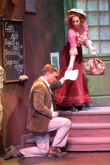 Mies polvistuu yhdelle polvelle ja kurottautuu seisovalle punahameiseen ja pipoon pukeutuneelle naiselle, joka ojentaa hänelle paperinpalasen. He ovat näyttämöllä, jonka taustalla on liitutaululla varustettu ruokalista ja ovi.