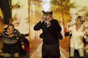 Kolme ihmistä esiintyy metsätaustan edessä; keskimmäisellä henkilöllä on susinaamio, kun taas kaksi muuta, jotka ovat pukeutuneet eläinkorvilla varustettuihin leikkimielisiin pukuihin, elehtivät eloisasti, ikään kuin näyttelisivät sadun kohtausta.